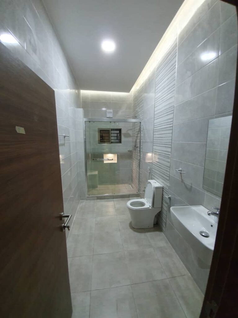Shower at end of the room with a toilet and sink with a mirror just above it